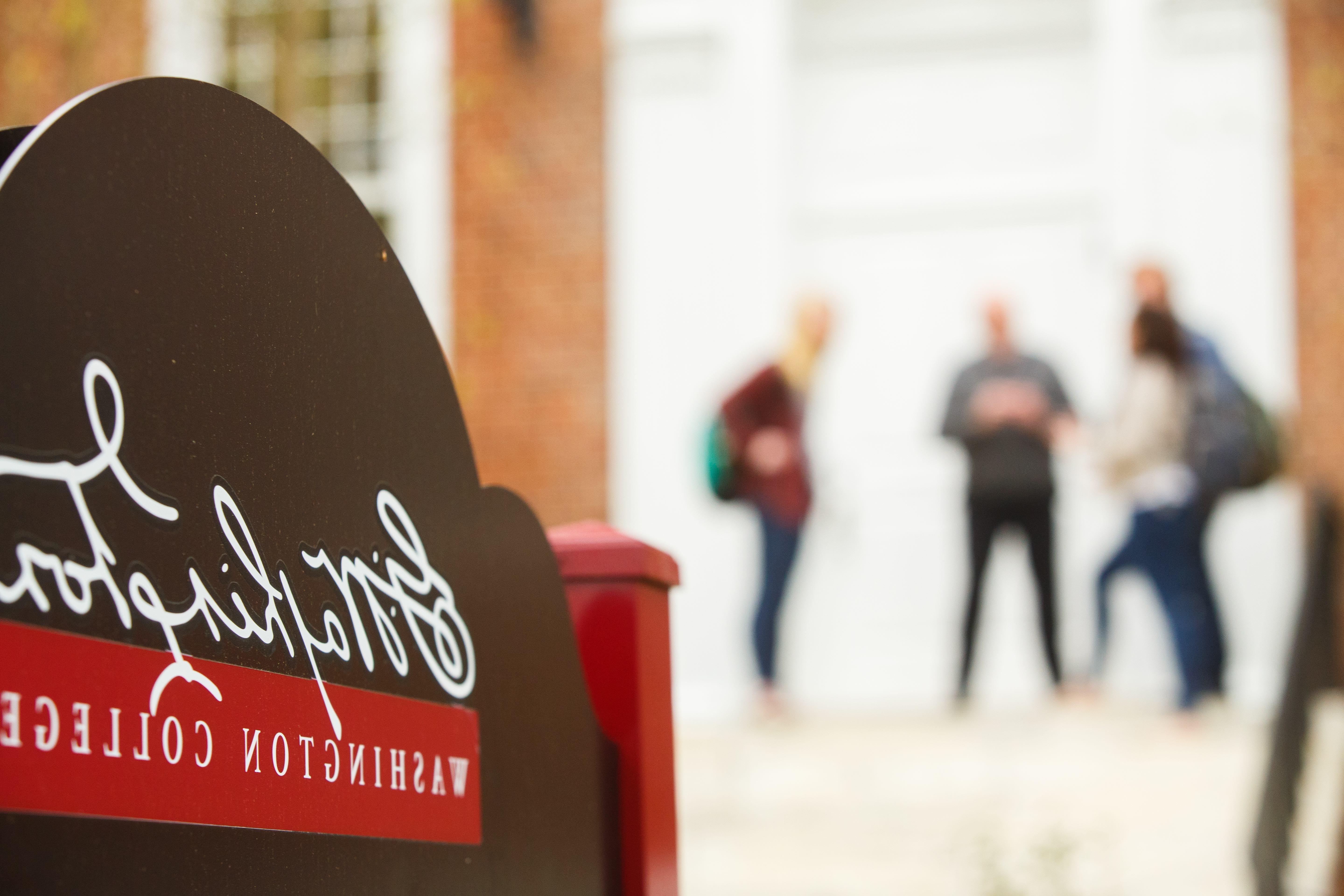 Sign for Washington College. Blurred in background, a group of students stand together.